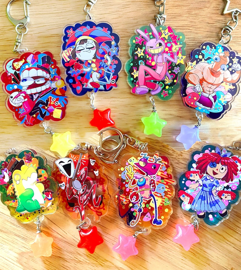 May include: A collection of colorful acrylic keychains featuring cartoon characters. Each keychain has a unique design with vibrant colors and is adorned with a star-shaped charm. The keychains are attached to silver-colored metal rings.