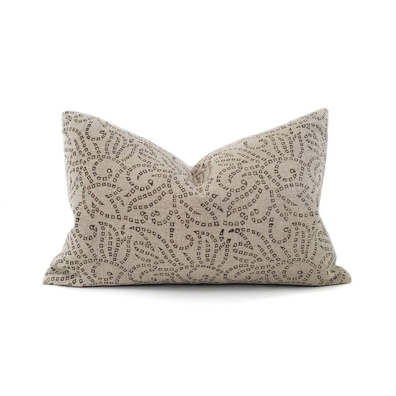 May include: A beige linen pillow with a brown swirl pattern. The pattern is made up of small circles and squares.