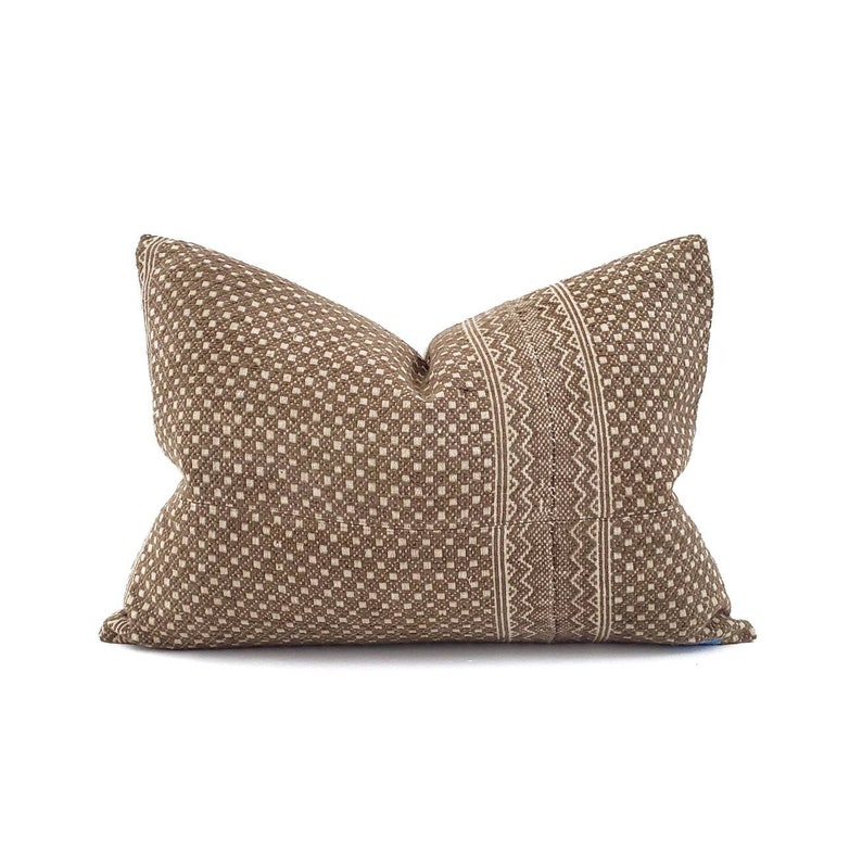 May include: A rectangular decorative pillow with a brown and beige geometric pattern. The pillow features a central vertical stripe with a detailed zigzag design, adding a textural contrast to the overall aesthetic. The pillow is designed for home decor.