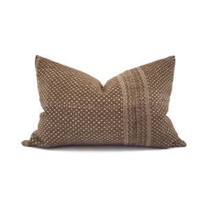 May include: A brown decorative pillow with a textured, dotted pattern. A vertical stripe with a zigzag design runs down the center. The pillow is rectangular and has a neutral color palette.