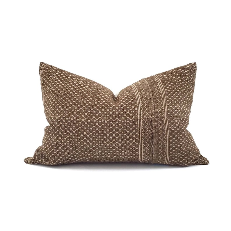 May include: A brown decorative pillow with a textured, dotted pattern. A vertical stripe with a zigzag design runs down the center. The pillow is rectangular and has a neutral color palette.