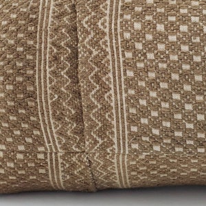 May include: Close-up of a textured pillow with a brown and cream woven pattern. The design features vertical stripes, geometric shapes, and a diamond pattern, creating a rustic aesthetic.