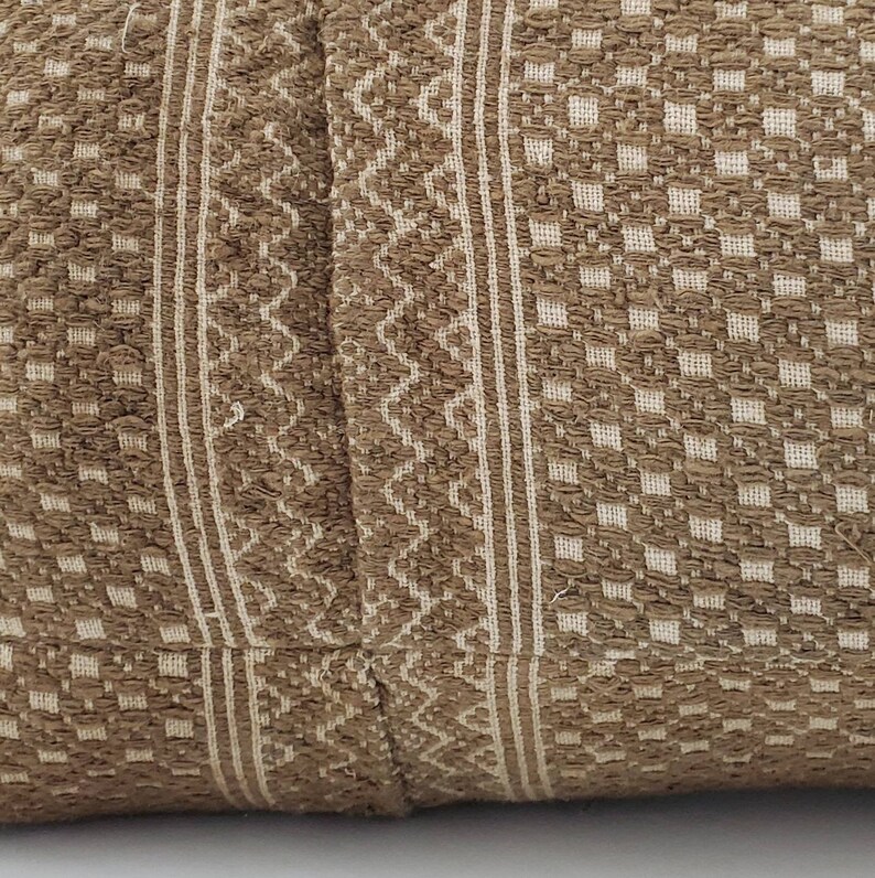 May include: Close-up of a textured pillow with a brown and cream woven pattern. The design features vertical stripes, geometric shapes, and a diamond pattern, creating a rustic aesthetic.