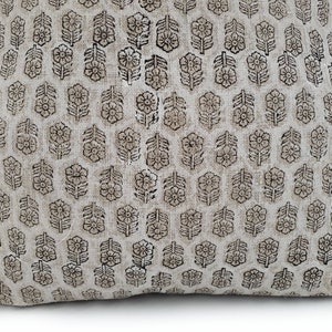 Puede incluir: Un coj&iacute;n beige con un patr&oacute;n repetitivo de dise&ntilde;os florales marrones. Las flores est&aacute;n estilizadas y dispuestas en forma de cuadr&iacute;cula, creando una apariencia texturizada. El coj&iacute;n tiene un aspecto suave y acogedor.