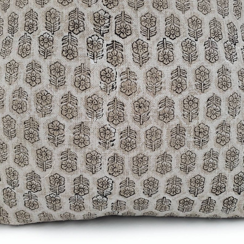 Puede incluir: Un coj&iacute;n beige con un patr&oacute;n repetitivo de dise&ntilde;os florales marrones. Las flores est&aacute;n estilizadas y dispuestas en forma de cuadr&iacute;cula, creando una apariencia texturizada. El coj&iacute;n tiene un aspecto suave y acogedor.