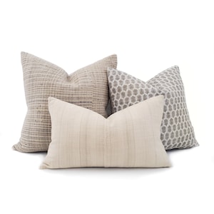 Puede incluir: Cuatro cojines decorativos en tonos neutros. Los cojines presentan varias texturas y patrones, incluyendo un dise&ntilde;o tejido, un estampado geom&eacute;trico y un patr&oacute;n de rayas. La paleta de colores incluye beige, gris y blanco roto.