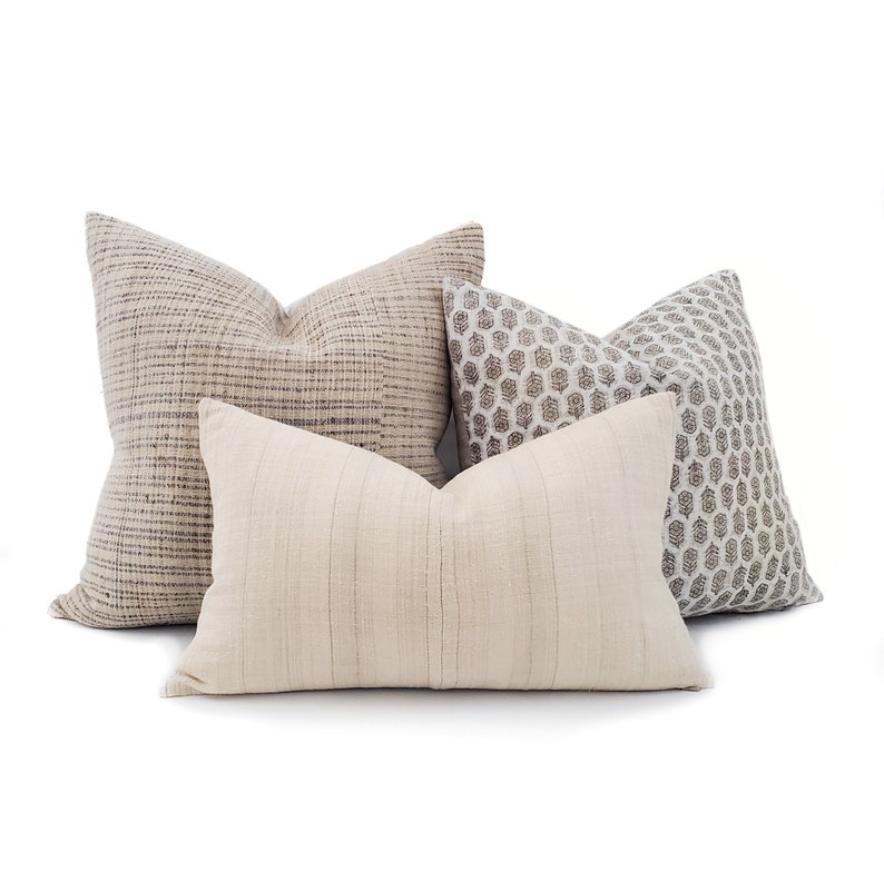 Puede incluir: Cuatro cojines decorativos en tonos neutros. Los cojines presentan varias texturas y patrones, incluyendo un dise&ntilde;o tejido, un estampado geom&eacute;trico y un patr&oacute;n de rayas. La paleta de colores incluye beige, gris y blanco roto.