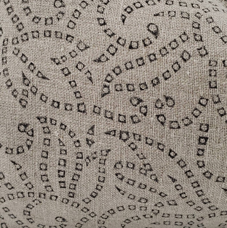 May include: A close-up of a beige fabric with a repeating pattern of black squares and diamonds. The fabric has a textured surface.