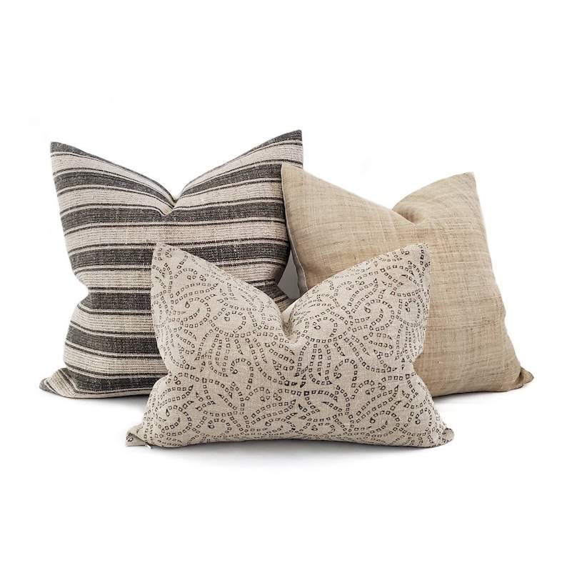 May include: Three decorative throw pillows. One pillow is striped in black and white, one is a solid beige, and the third is beige with a black swirl pattern.