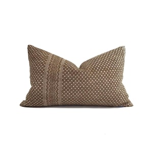 May include: A brown lumbar pillow with a geometric pattern. The pillow features a central vertical stripe with a zig-zag design and a dotted pattern on the rest of the pillow. The pillow is rectangular and has a soft, textured appearance.