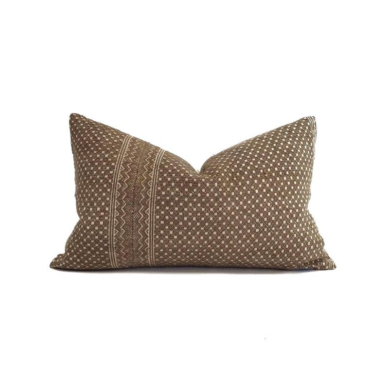 May include: A brown lumbar pillow with a geometric pattern. The pillow features a central vertical stripe with a zig-zag design and a dotted pattern on the rest of the pillow. The pillow is rectangular and has a soft, textured appearance.