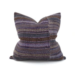 May include: A striped throw pillow with a brown, purple, and gray color scheme. The pillow is made of a woven fabric with a slightly distressed look.