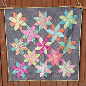 May include: A quilt with a gray background and a pattern of colorful pinwheels. The pinwheels are made of various fabrics with floral patterns in shades of pink, teal, yellow, and orange.