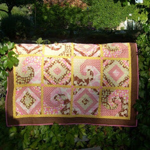 May include: A patchwork quilt with a brown, pink, and yellow color scheme. The quilt is made up of squares with different patterns, including floral, geometric, and paisley designs.