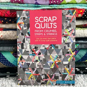 May include: A book titled "SCRAP QUILTS" with the subtitle "FROM CRUMBS, STRIPS & STRINGS" is displayed. The cover features a geometric patchwork design in shades of gray, black, and white, accented with colorful strips. The book is by Emily Bailey.