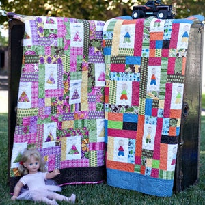May include: Two colorful patchwork quilts with a whimsical design featuring stick figures. The quilts are displayed on a wooden chest with a toy truck on top.