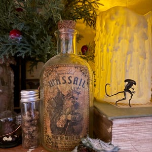 Pu&ograve; includere: Una bottiglia in vetro trasparente con tappo in sughero e un'etichetta in stile vintage con la scritta Tainted WASSAIL, OLD SPIRITS CO., North Pole Div., 100 PROOF, raffigurante una figura scheletrica con corona e un bastone.