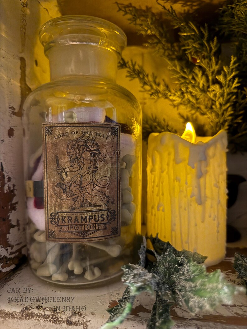 Pu&ograve; includere: Un barattolo da farmacia in vetro trasparente con tappo in vetro, contenente piccoli oggetti bianchi a forma di osso. Un'etichetta rettangolare sul davanti presenta un'illustrazione di Krampus e il testo: Lord of the Yule, Krampus Potion.