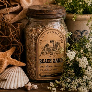 Op de afbeelding: Een glazen pot gevuld met strandzand, afgesloten met een donker, verweerd metalen deksel. De pot is voorzien van een vintage-stijl etiket met de tekst Quality Souvenir Brand, Beach Sand, Locale: Revere Beach en Date: July 7, 1861, met illustratie.
