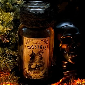 Pu&ograve; includere: Una bottiglia di vetro trasparente con un rivestimento in tessuto nero attorno al collo, dotata di un'etichetta rettangolare con la scritta Tainted WASSAIL OLD SPIRITS CO. BOTTLERS & DISTILLERY NORTH POLE DIV 100 PROOF e un'illustrazione di una figura barbuta.