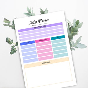 Könnte beinhalten: Ein druckbarer Tagesplaner mit Abschnitten für "Must Get Done Today", "To Do List", "Termine/Meetings", "Anrufe" und "Notizen und Kritzeleien". Der Planer ist in einem hellvioletten, rosa und blauen Farbschema gestaltet.