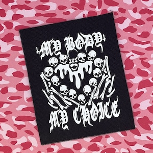 May include: Black iron-on patch with white text and graphic. The text reads "My Body My Choice" and the graphic is a circle of skulls with bones and dripping liquid.
