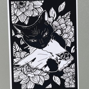 May include: Black and white illustration of a cat with its head peeking out from behind a hand with a rose tattoo. The image is surrounded by stylized flowers.