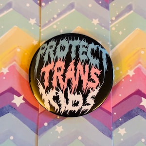 May include: Black button with the words "Protect Trans Kids" in white, pink, and blue stylized lettering.