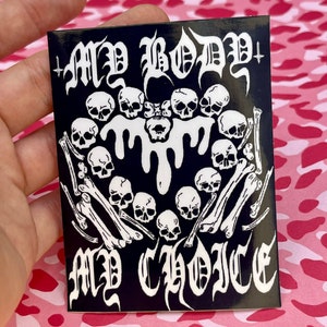 Peut inclure: Autocollant noir avec texte blanc et illustrations. Le texte dit "MY BODY MY CHOICE" en lettres gothiques. Le design comprend des crânes, des os et un effet dégoulinant.