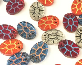 May include: Assortment of oval-shaped glass buttons with various geometric designs in red, orange, blue, and silver. The buttons have two holes each.