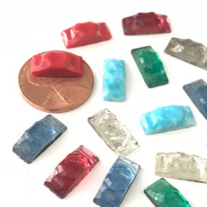 May include: Assortment of small, rectangular, faceted glass tiles in various colors, including red, blue, green, and clear. The tiles are approximately the size of a US penny.