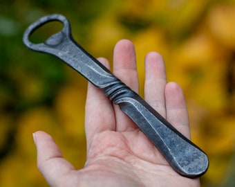 May include: A hand holds a black metal bottle opener with a twisted handle. The opener has a classic design and is made of durable metal.