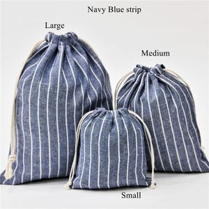 Könnte beinhalten: Drei gestreifte Kordelbeutel in verschiedenen Größen: groß, mittel und klein. Die Beutel sind aus blau-weiß gestreiftem Stoff. Der Text "Navy Blue strip" befindet sich oben im Bild. Der Text "Large" befindet sich über dem größten Beutel. Der Text "Medium" befindet sich über dem mittelgroßen Beutel. Der Text "Small" befindet sich unter dem kleinsten Beutel.