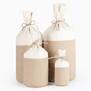 Op de afbeelding: Vier verschillende maten jute- en canvas-cadeauzakken met een natuurlijke touwband. De zakken zijn allemaal wit met een jutebodem.
