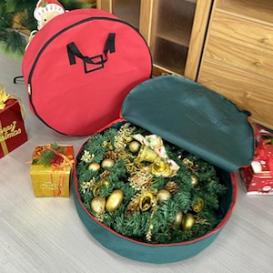 May include: Two round Christmas wreath storage bags. One bag is red with a black handle and the other bag is green with a black handle. The green bag is open and a wreath is inside.
