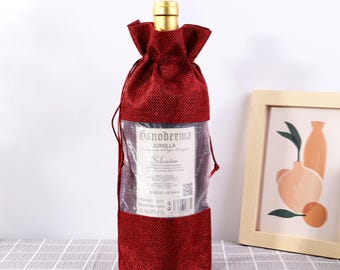 May include: Red burlap wine bottle bag with a clear plastic window showing a bottle of wine with a label that reads "Ganoderma Jumilla Seleccion".