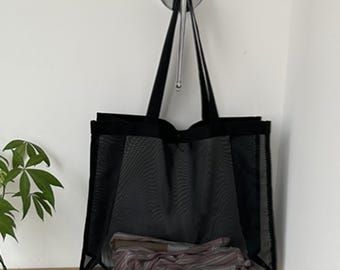 May include: Black mesh tote bag with black handles. The bag is hanging on a hook and has a folded piece of fabric inside.