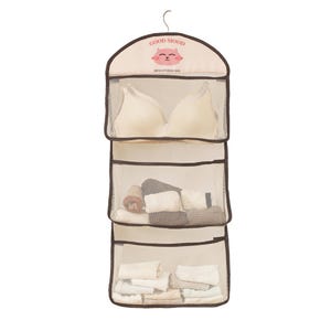 Peut inclure: Organisateur suspendu beige avec trois compartiments en maille. Le compartiment supérieur contient un soutien-gorge, le compartiment du milieu contient des chaussettes enroulées et le compartiment inférieur contient des sous-vêtements pliés. L'organisateur a une bordure brune et un graphique de chat rose avec le texte "GOOD MOOD" et "MESH STORAGE BAG".