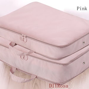 Puede incluir: Una bolsa de almacenamiento plegable de color rosa con dos compartimentos y dos asas. La bolsa está hecha de un material suave y duradero y es perfecta para guardar ropa, mantas u otros artículos.