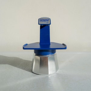 Op de afbeelding: Een zilveren en blauwe Gemini Express koffiezetapparaat met een blauwe handgreep en een blauwe basis. De koffiezetapparaat heeft een label met de tekst "GEMINI EXPRESS ITALY".
