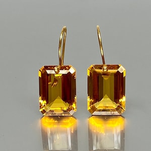 May include: A pair of gold earrings featuring large, faceted, emerald-cut topaz gemstones. The gemstones are a warm, honey-amber colour.