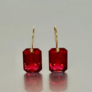 May include: A pair of gold hoop earrings with red gemstone drops. The gemstones are faceted and have a square shape.