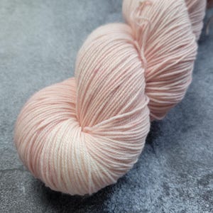 May include: A skein of soft, pale pink yarn. The yarn is tightly wound, showing the individual strands. The color is a delicate, light pink, with subtle variations in tone. The yarn appears to be smooth and fine, suitable for knitting or crocheting projects.