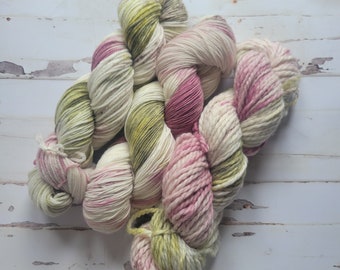 May include: A skein of chunky yarn in shades of cream, pink, and green. The yarn is thick and textured, with a soft, inviting appearance. The colors are blended, creating a visually appealing and unique look. Ideal for knitting or crocheting projects.