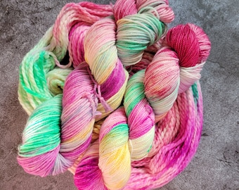 May include: A skein of colorful yarn in shades of pink, green, yellow, and purple. The yarn is tightly wound and appears soft, with a gradient effect. Ideal for knitting or crochet projects.