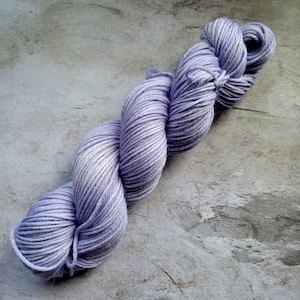 May include: A skein of lavender and white yarn, twisted and arranged on a mottled gray surface. The yarn is tightly wound, showing the individual strands and color variations. Ideal for knitting or crochet projects.