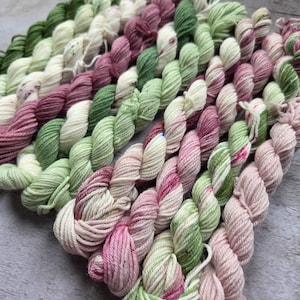 May include: A collection of mini yarn skeins in various shades of green, pink, and cream. The yarn is arranged in neat rows, showcasing the different color combinations and textures. Ideal for knitting or crochet projects.