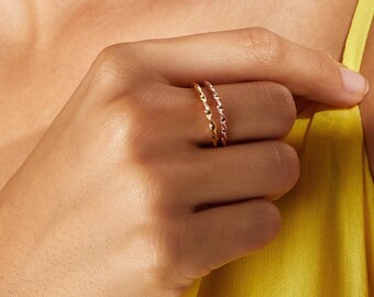 May include: Two gold rings, one with a twisted design and the other with a smooth finish, worn on a finger.
