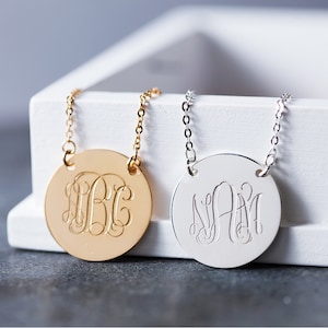 May include: Two gold and silver necklaces with round pendants featuring engraved monograms. The gold necklace has the monogram "B.B.C." and the silver necklace has the monogram "N.A.M."