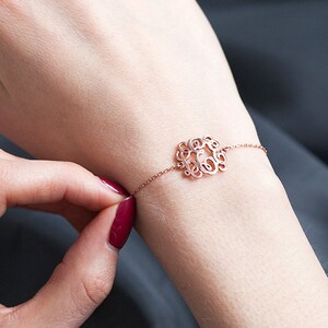 May include: A rose gold bracelet featuring a delicate, circular monogram charm. The charm is crafted from intertwined letters.